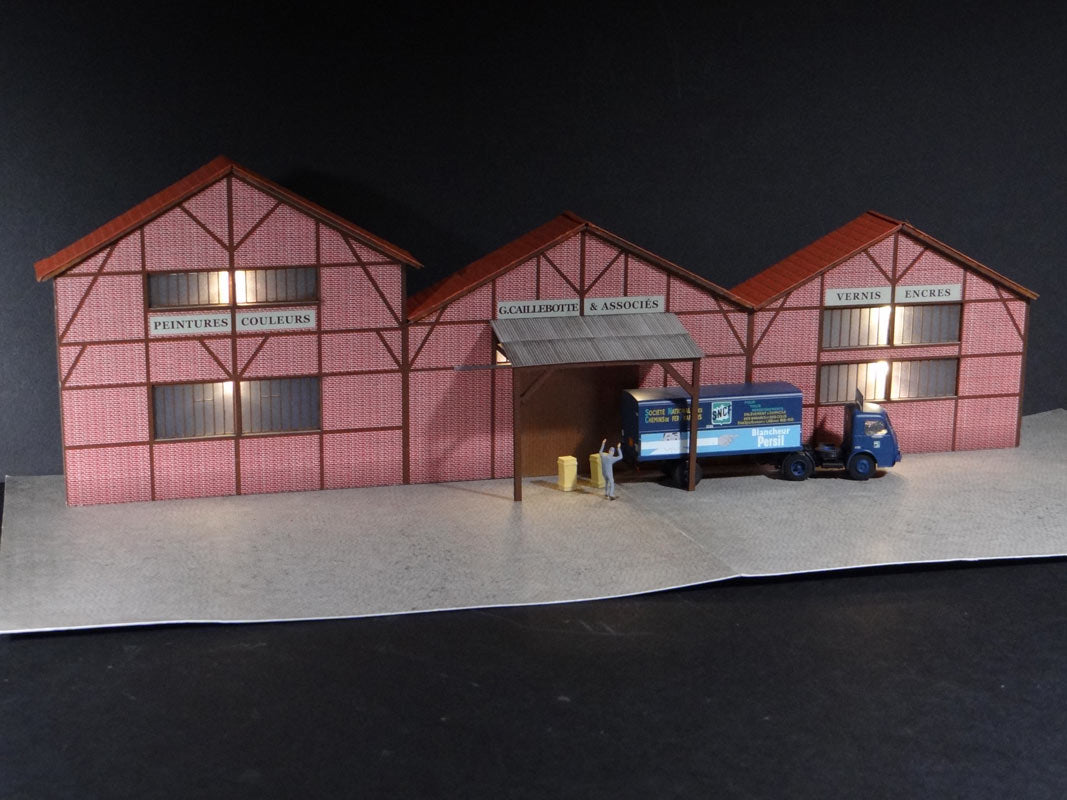Fond de décor en relief d´une usine avec baies éclairées "Grossiste Peinture Vernis"